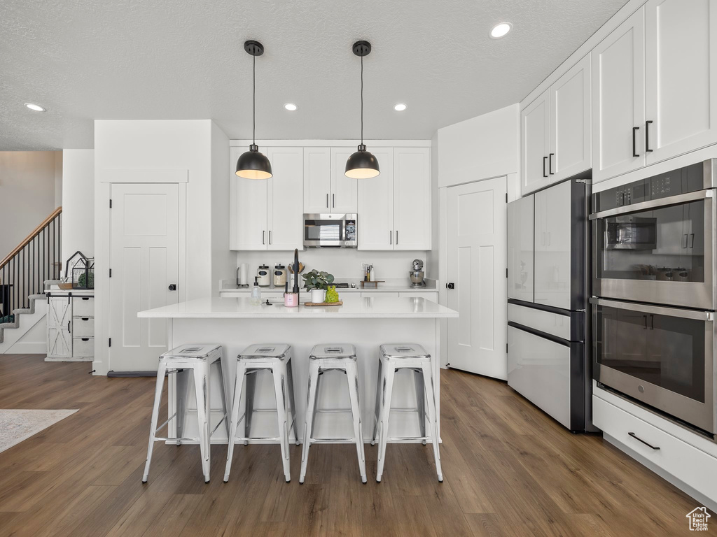 Kitchen featuring dark hardwood / wood-style floors, stainless steel appliances, white cabinets, and an island with sink