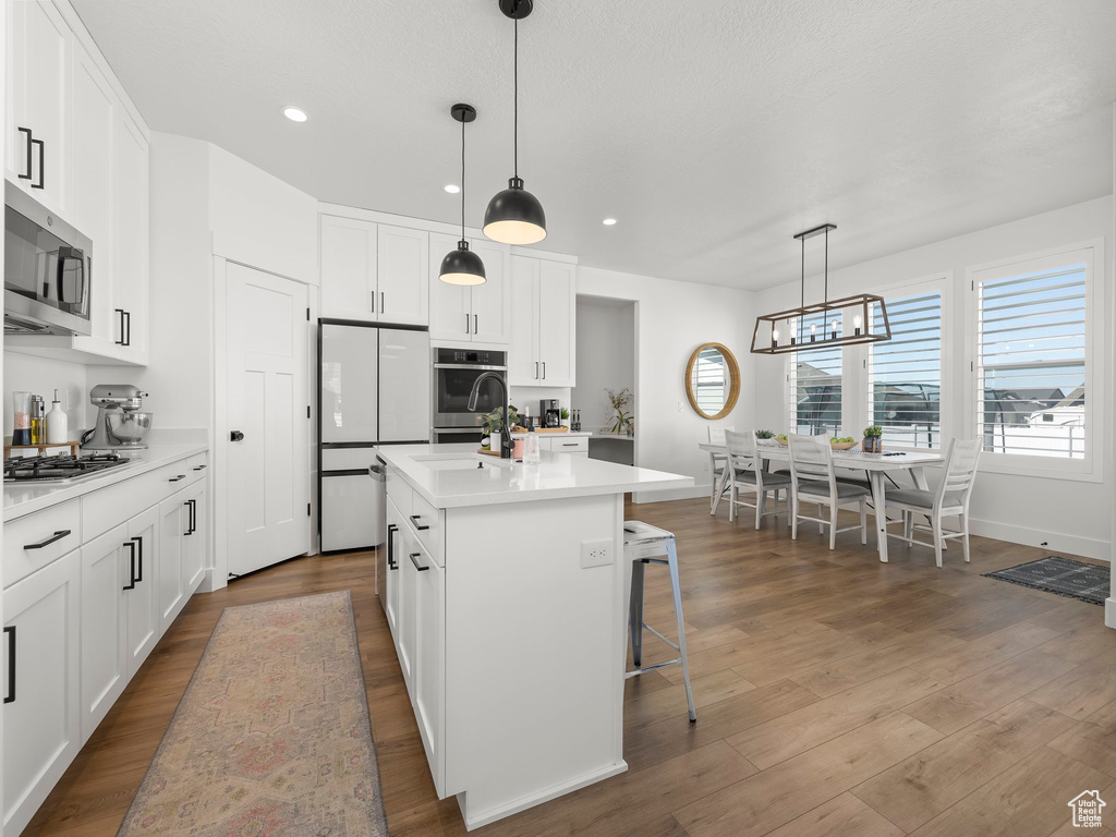 Kitchen with a center island with sink, dark wood-type flooring, stainless steel appliances, and pendant lighting