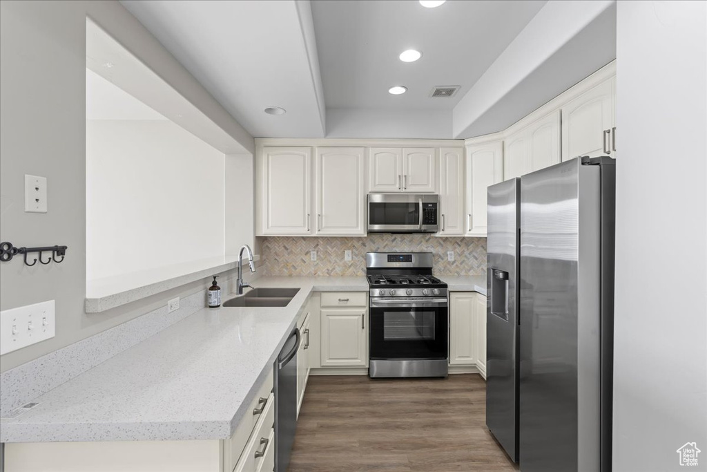 Kitchen with dark hardwood / wood-style flooring, appliances with stainless steel finishes, tasteful backsplash, white cabinetry, and sink