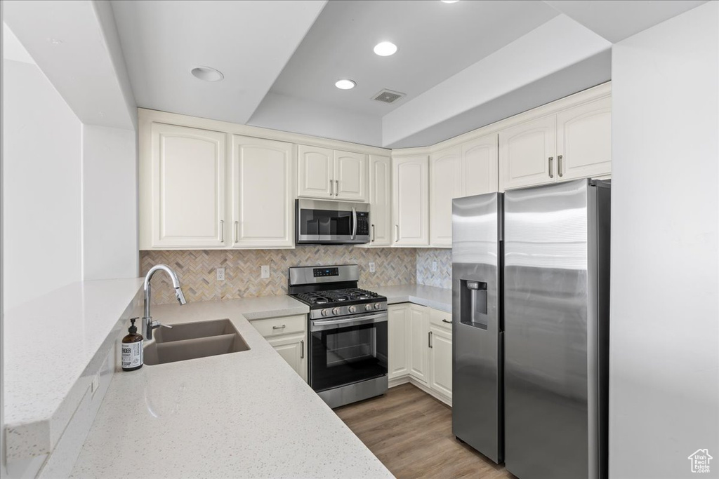 Kitchen featuring appliances with stainless steel finishes, dark hardwood / wood-style floors, light stone countertops, backsplash, and sink