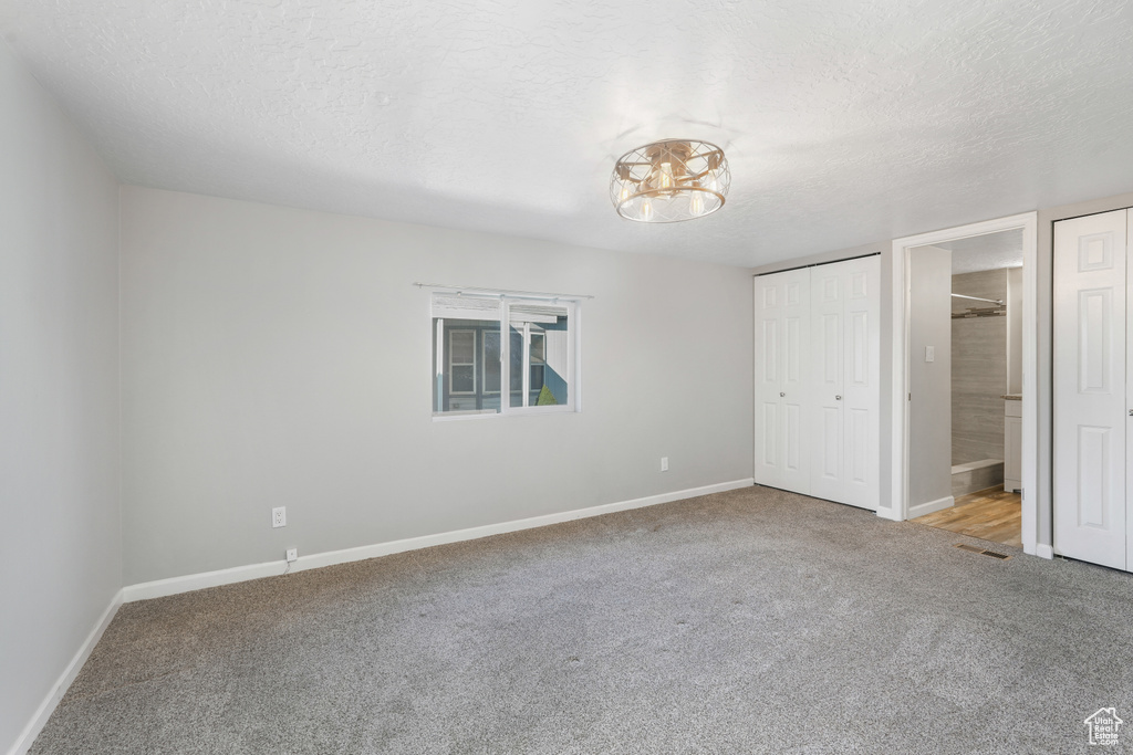 Unfurnished bedroom with ensuite bath, light colored carpet, and a textured ceiling