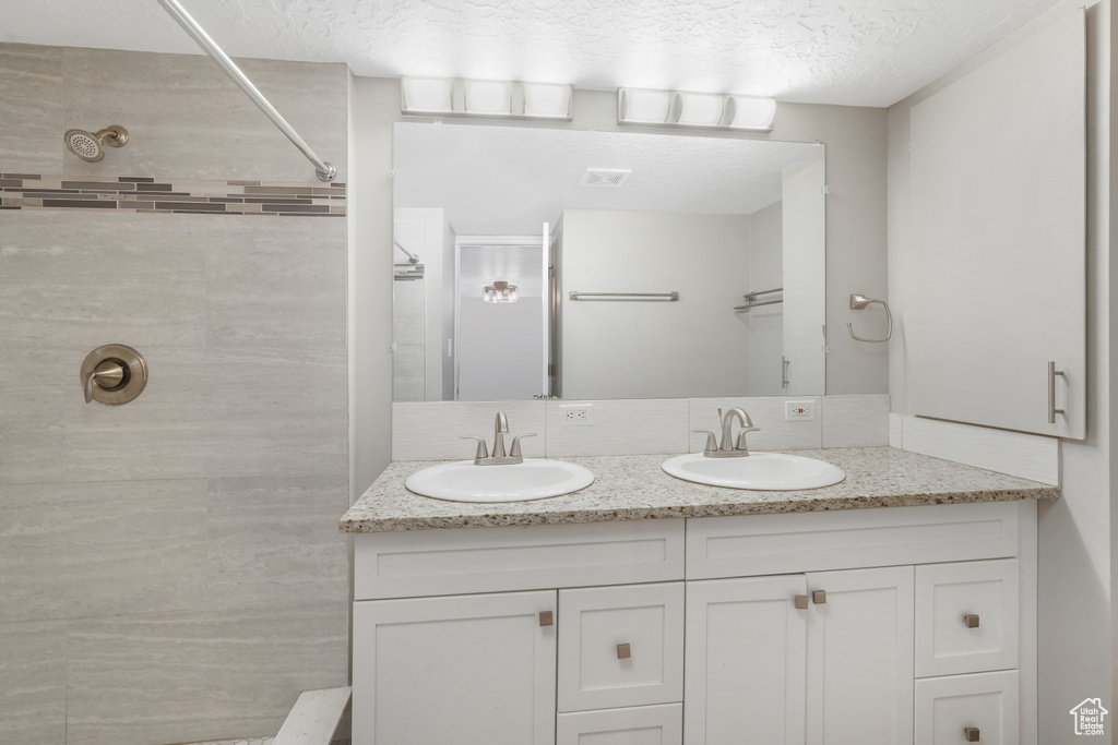 Bathroom featuring dual sinks, a textured ceiling, and large vanity