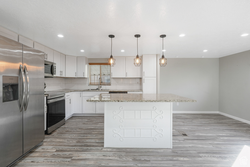 Kitchen with appliances with stainless steel finishes, light hardwood / wood-style flooring, white cabinetry, and backsplash