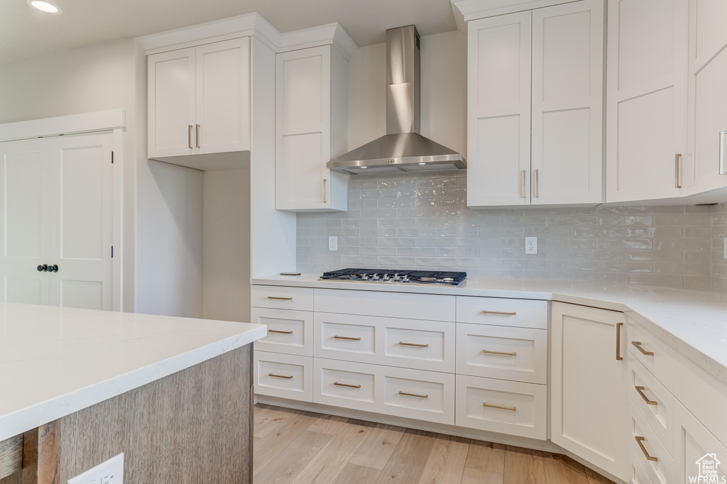Kitchen featuring white cabinets, backsplash, light wood-type flooring, and wall chimney exhaust hood