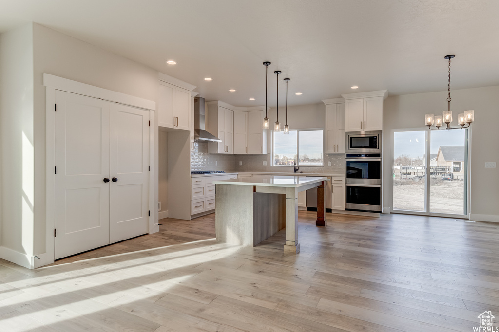 Kitchen featuring white cabinetry, wall chimney range hood, appliances with stainless steel finishes, and light hardwood / wood-style floors