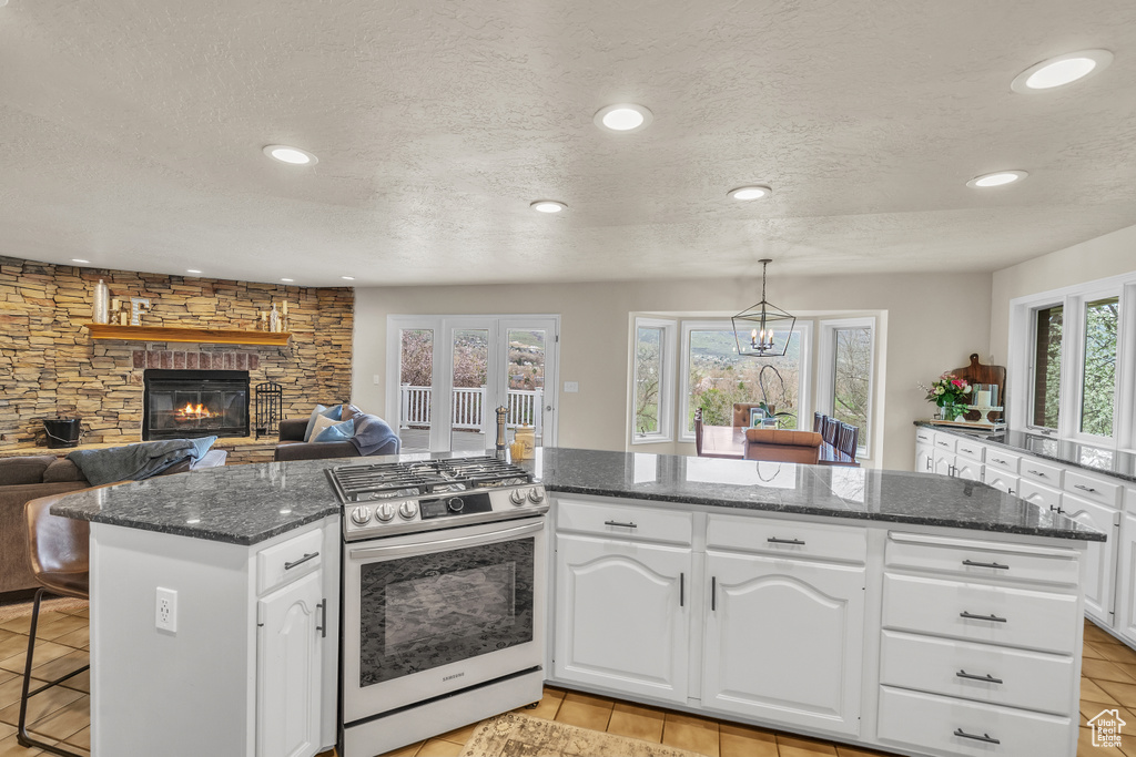 Kitchen with gas range oven, a healthy amount of sunlight, white cabinets, and a stone fireplace