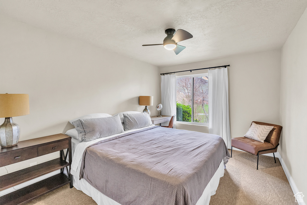 Bedroom with ceiling fan, light colored carpet, and a textured ceiling