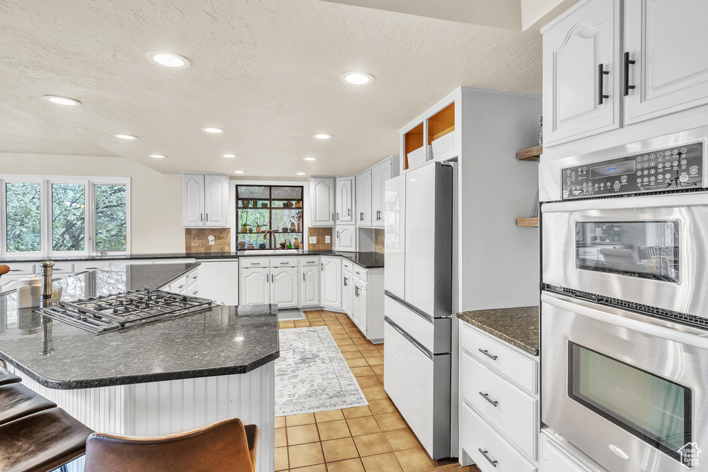 Kitchen with white cabinets, a wealth of natural light, tasteful backsplash, and stainless steel appliances