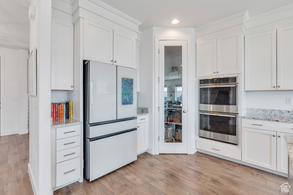 Kitchen with light stone counters, white fridge, light hardwood / wood-style floors, stainless steel double oven, and white cabinets