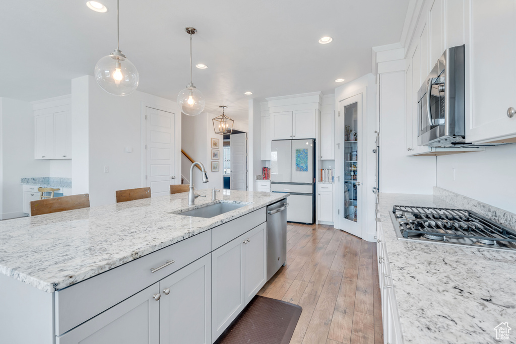 Kitchen with appliances with stainless steel finishes, hanging light fixtures, light hardwood / wood-style floors, sink, and a center island with sink