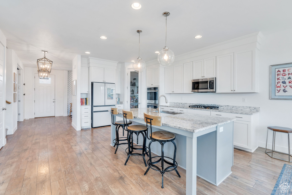 Kitchen featuring white cabinets, appliances with stainless steel finishes, a notable chandelier, pendant lighting, and light hardwood / wood-style flooring