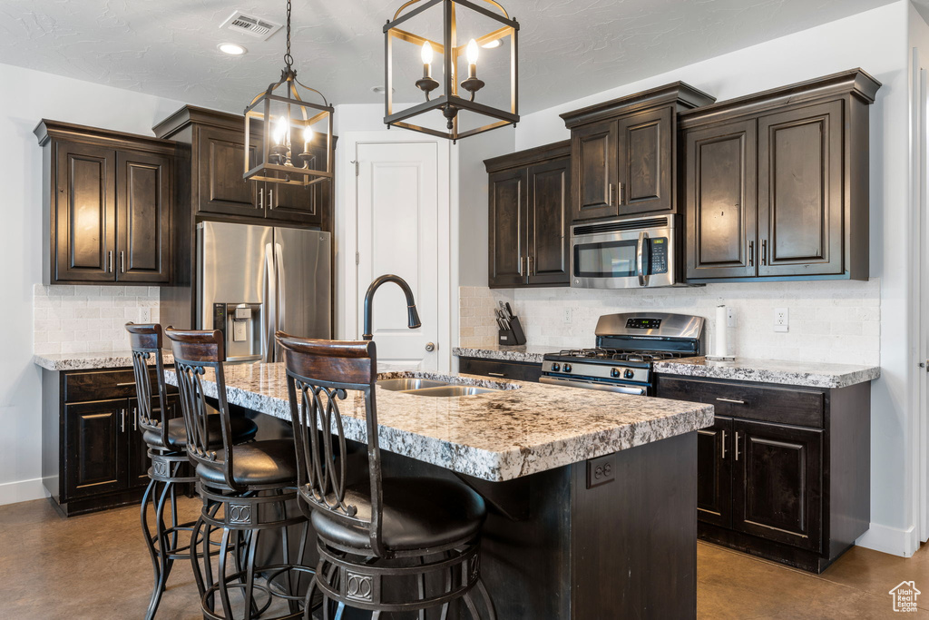 Kitchen featuring a breakfast bar, appliances with stainless steel finishes, tasteful backsplash, an island with sink, and hanging light fixtures