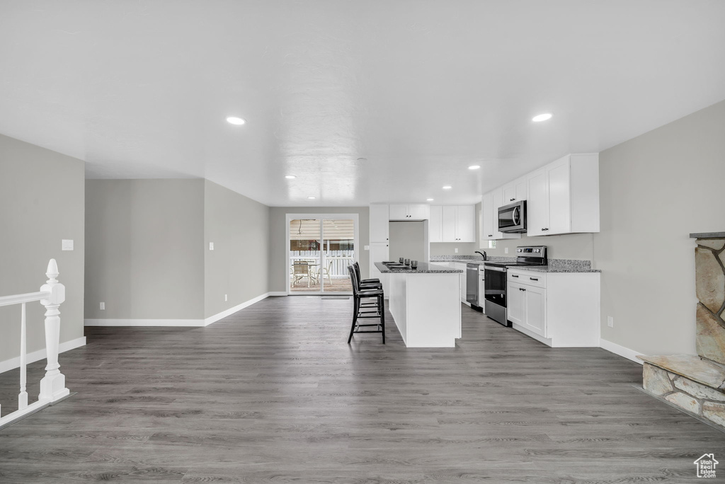 Kitchen with appliances with stainless steel finishes, hardwood / wood-style floors, a breakfast bar area, and white cabinets