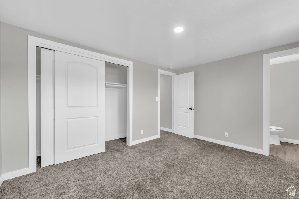 Unfurnished bedroom featuring a closet, dark carpet, and ensuite bathroom