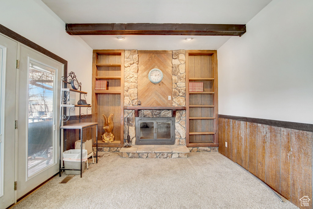 Living room featuring a stone fireplace, beamed ceiling, and light carpet