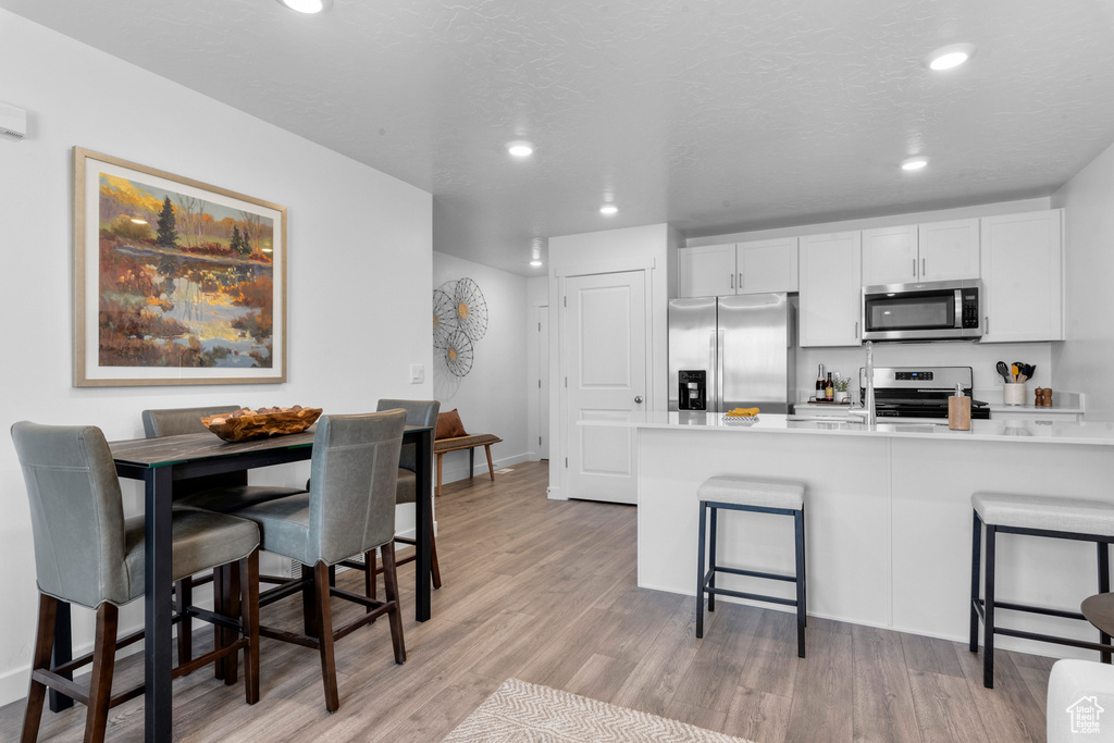 Kitchen featuring a kitchen bar, light hardwood / wood-style floors, stainless steel appliances, and white cabinetry