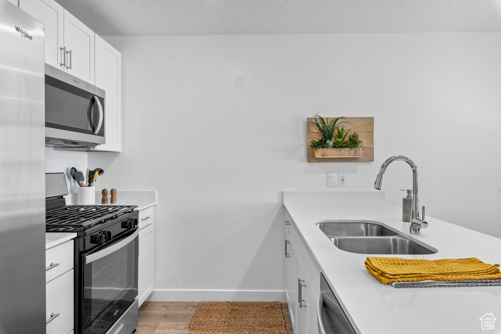 Kitchen featuring appliances with stainless steel finishes, white cabinets, light wood-type flooring, and sink