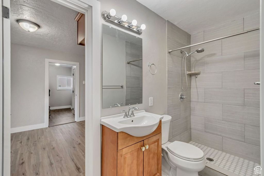 Bathroom with large vanity, a textured ceiling, tiled shower, toilet, and hardwood / wood-style flooring