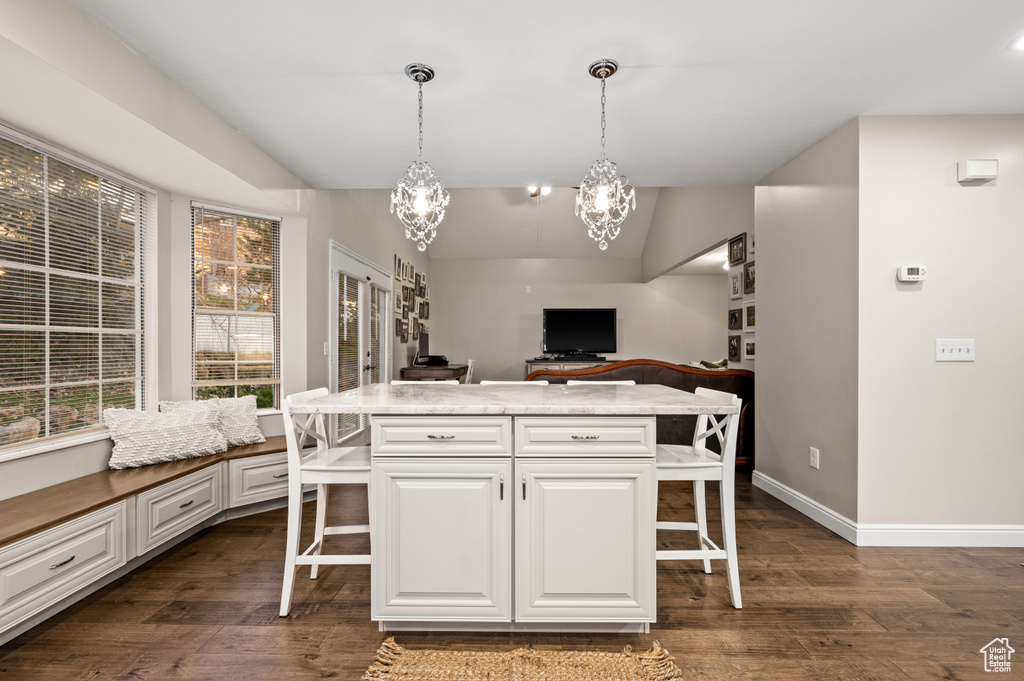 Kitchen with white cabinets, dark hardwood / wood-style floors, a notable chandelier, pendant lighting, and a kitchen breakfast bar
