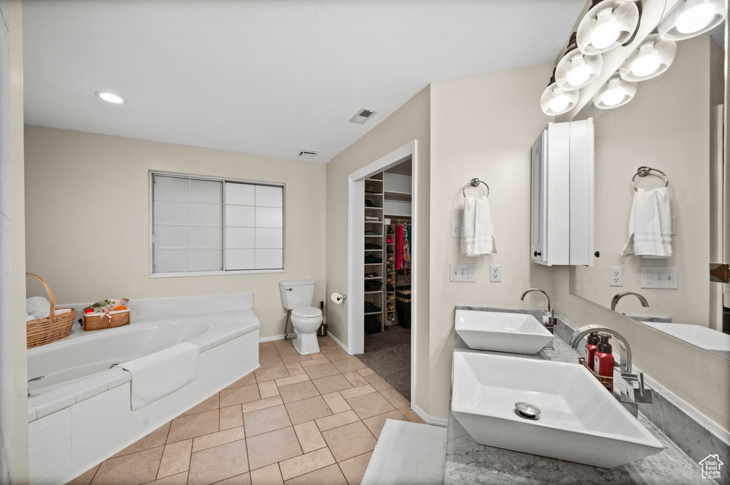Bathroom featuring dual vanity, tile floors, toilet, and a washtub