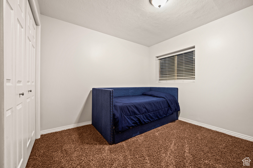 Bedroom with a textured ceiling, dark colored carpet, and a closet