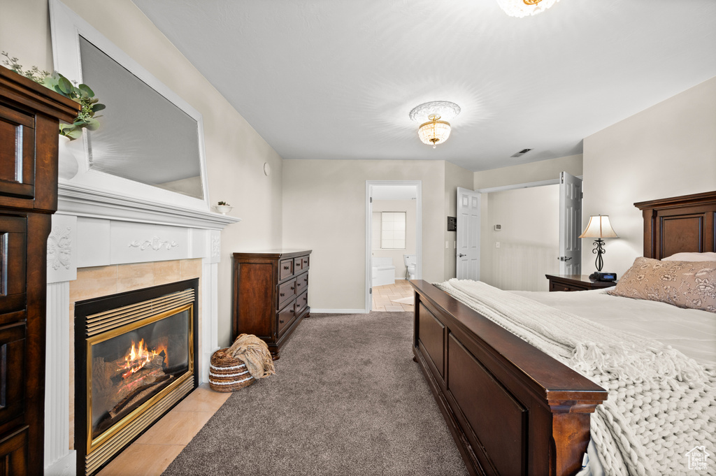 Carpeted bedroom featuring connected bathroom and a tile fireplace