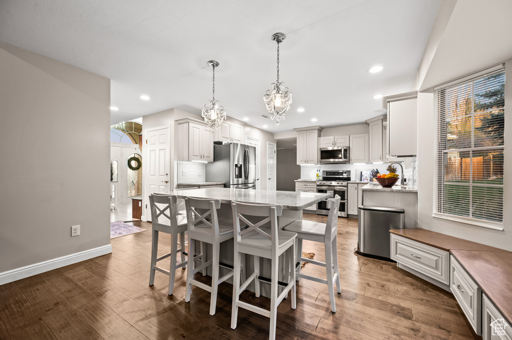 Kitchen with white cabinets, appliances with stainless steel finishes, dark hardwood / wood-style flooring, pendant lighting, and light stone counters
