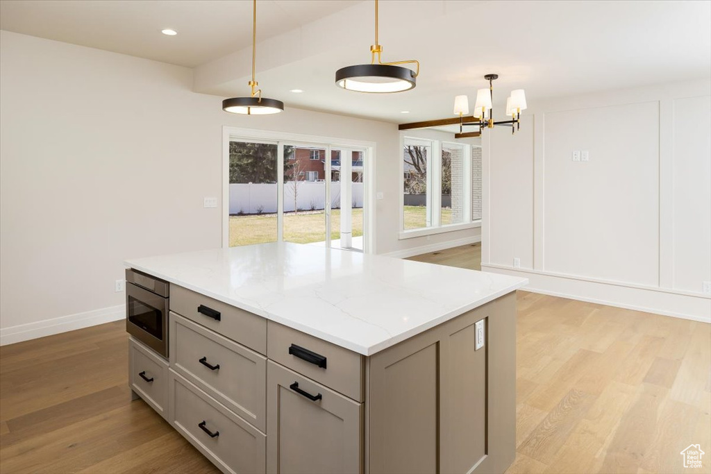 Kitchen featuring decorative light fixtures, an inviting chandelier, light hardwood / wood-style floors, gray cabinets, and stainless steel microwave