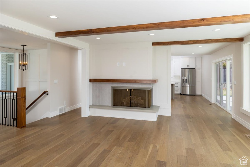 Unfurnished living room featuring beam ceiling, a chandelier, and light hardwood / wood-style flooring