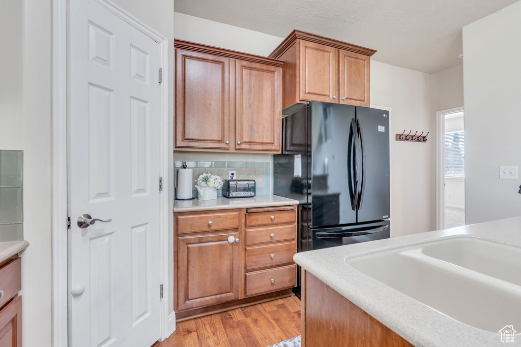 Kitchen with sink, black refrigerator, light hardwood / wood-style floors, and tasteful backsplash