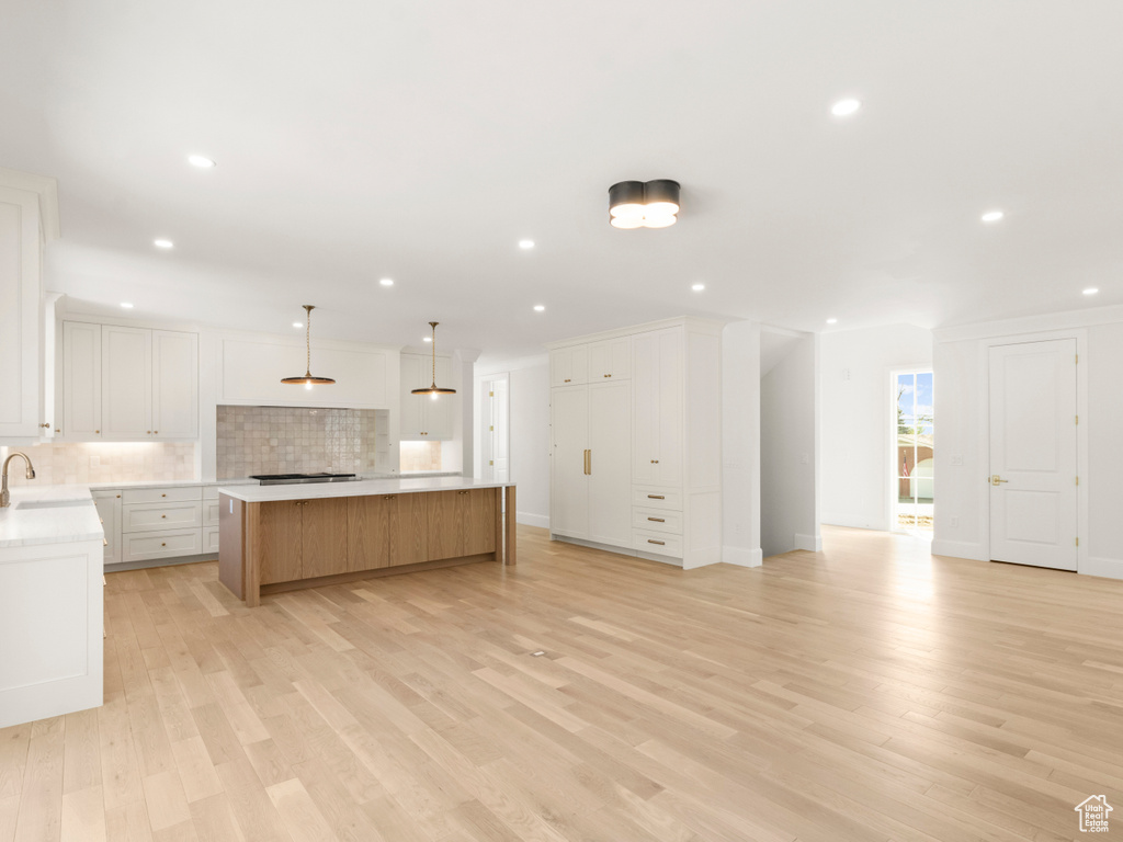 Kitchen featuring a center island, tasteful backsplash, white cabinetry, light hardwood / wood-style flooring, and pendant lighting