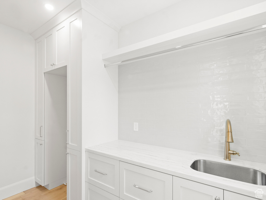 Interior space featuring white cabinets, sink, light hardwood / wood-style floors, tasteful backsplash, and light stone countertops