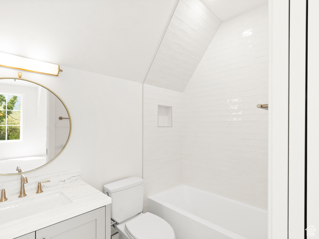 Full bathroom featuring tiled shower / bath, toilet, vanity, and vaulted ceiling