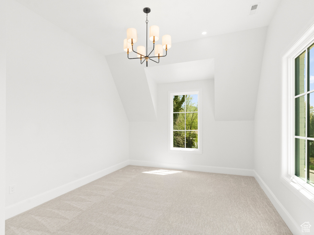 Spare room with lofted ceiling, plenty of natural light, carpet flooring, and an inviting chandelier