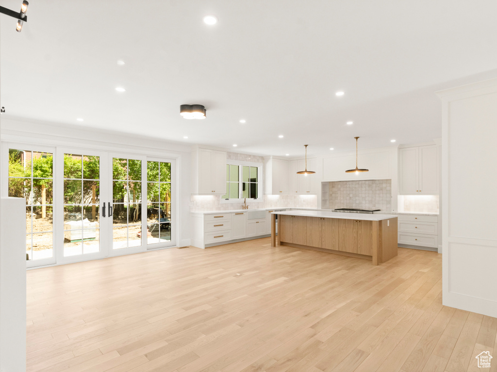 Kitchen with light wood-type flooring, a center island, white cabinetry, and tasteful backsplash