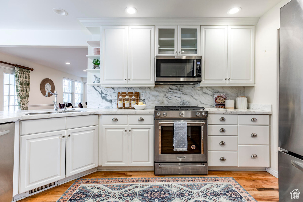 Kitchen featuring tasteful backsplash, white cabinets, stainless steel appliances, light hardwood / wood-style flooring, and sink