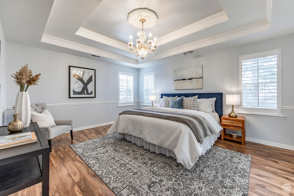 Bedroom featuring an inviting chandelier, ornamental molding, hardwood / wood-style floors, and a raised ceiling