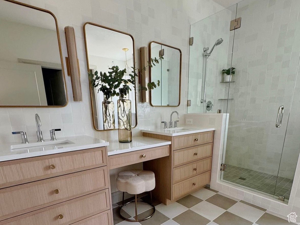 Bathroom featuring a shower with shower door, backsplash, dual vanity, and tile floors