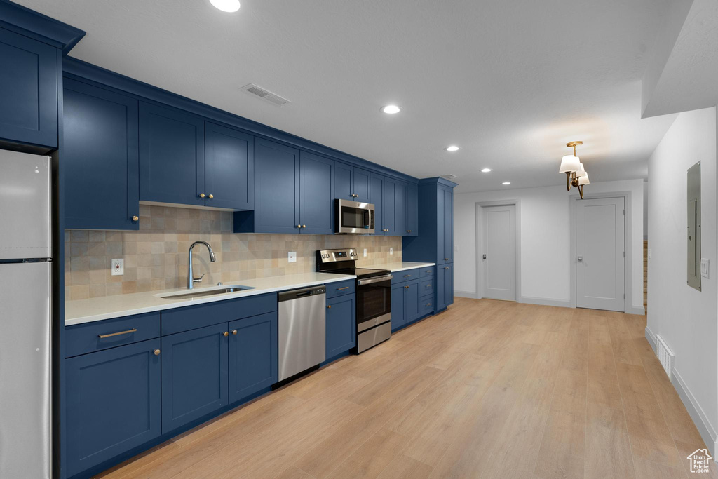 Kitchen with blue cabinetry, light hardwood / wood-style flooring, appliances with stainless steel finishes, and sink