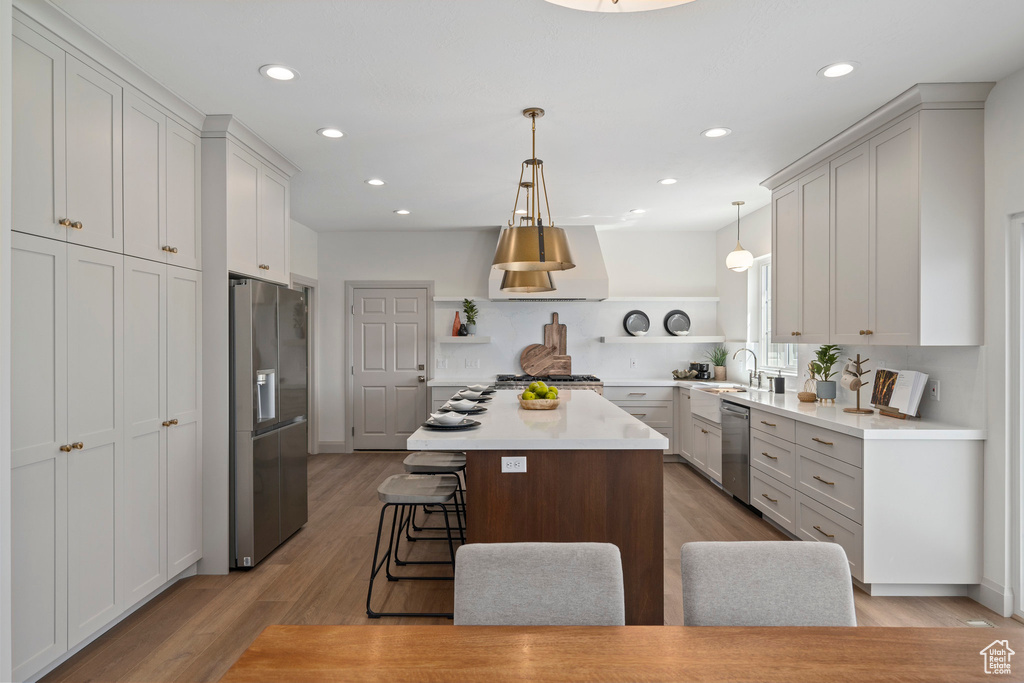 Kitchen featuring a center island, a breakfast bar area, stainless steel appliances, light hardwood / wood-style flooring, and wall chimney exhaust hood