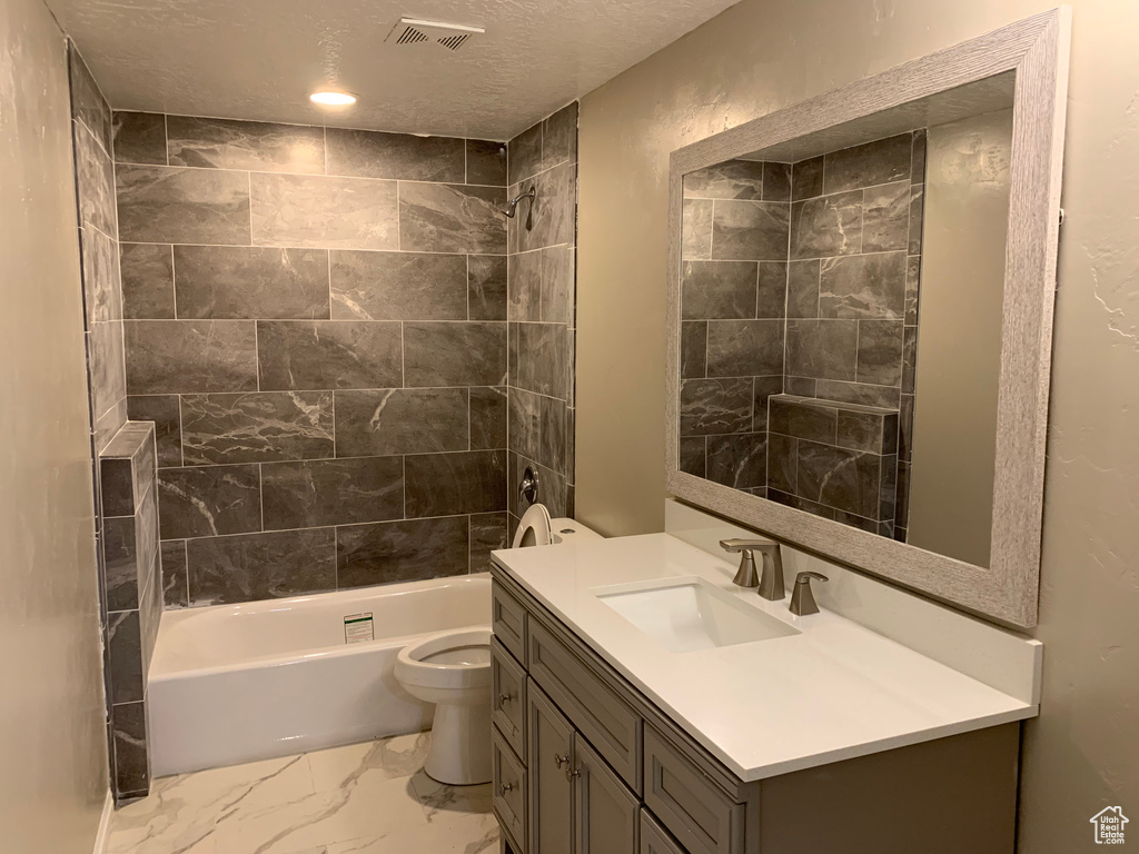 Full bathroom with tile floors, toilet, tiled shower / bath combo, and vanity with extensive cabinet space