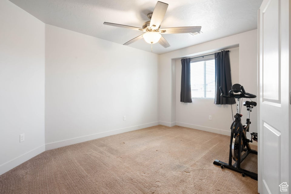 Exercise room with ceiling fan and light colored carpet