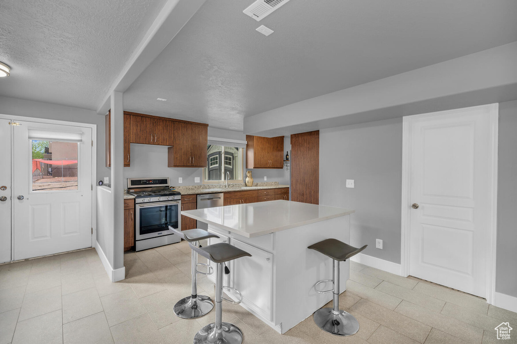 Kitchen featuring a textured ceiling, appliances with stainless steel finishes, light tile flooring, and a kitchen breakfast bar