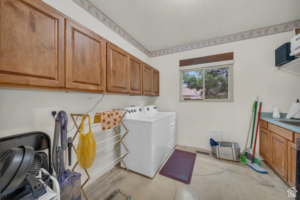 Clothes washing area featuring sink, cabinets, washer and clothes dryer, and a textured ceiling