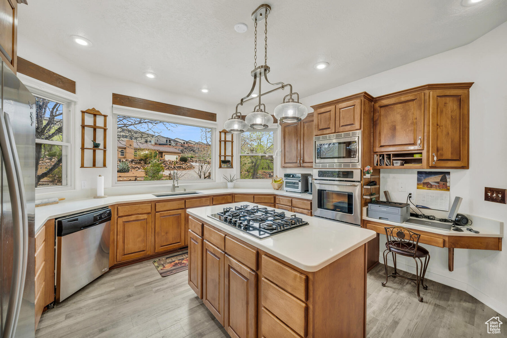 Kitchen featuring light wood-type flooring, a center island, stainless steel appliances, decorative light fixtures, and sink