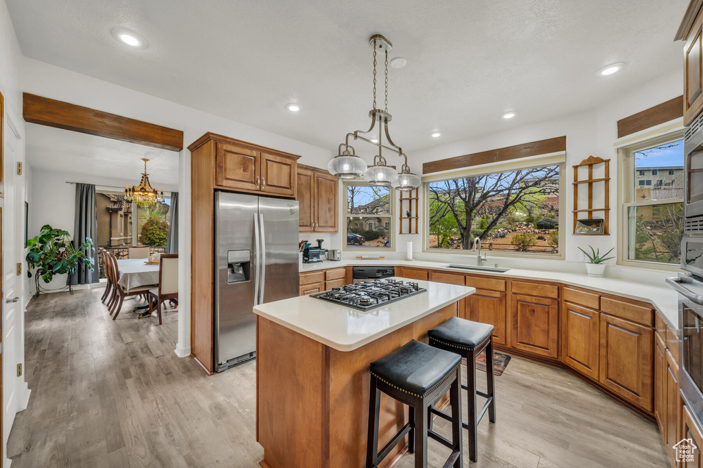 Kitchen featuring appliances with stainless steel finishes, light hardwood / wood-style floors, a kitchen island, a kitchen bar, and sink