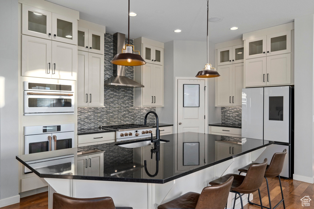 Kitchen with hanging light fixtures, an island with sink, and wall chimney exhaust hood