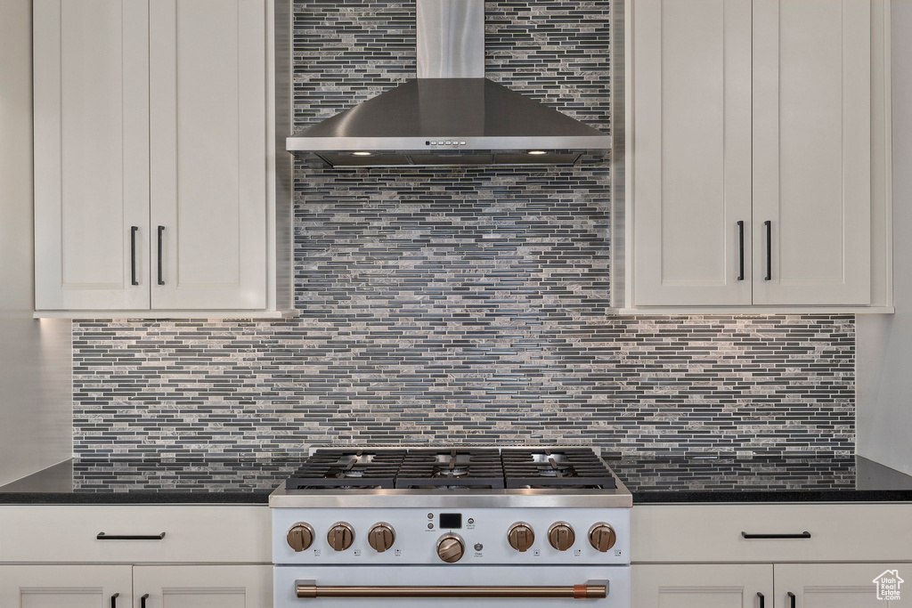 Kitchen featuring wall chimney exhaust hood, white cabinets, and tasteful backsplash