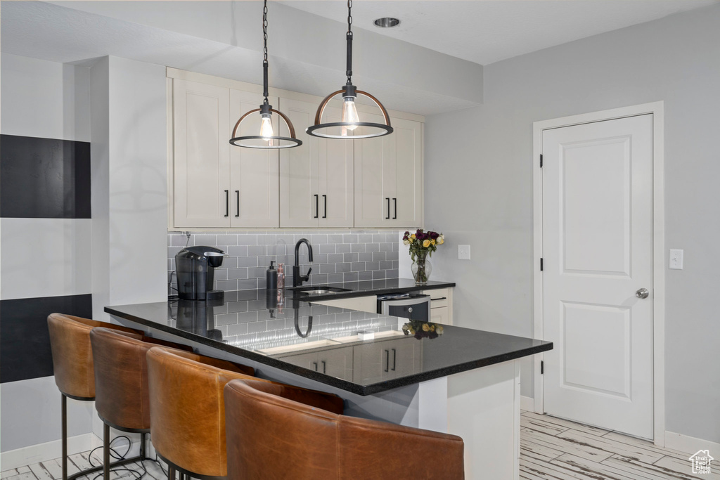 Kitchen with tasteful backsplash, white cabinets, hanging light fixtures, kitchen peninsula, and sink