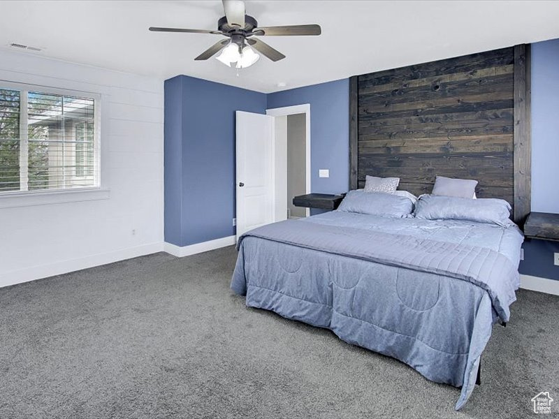 Bedroom with ceiling fan, dark carpet, and wooden walls